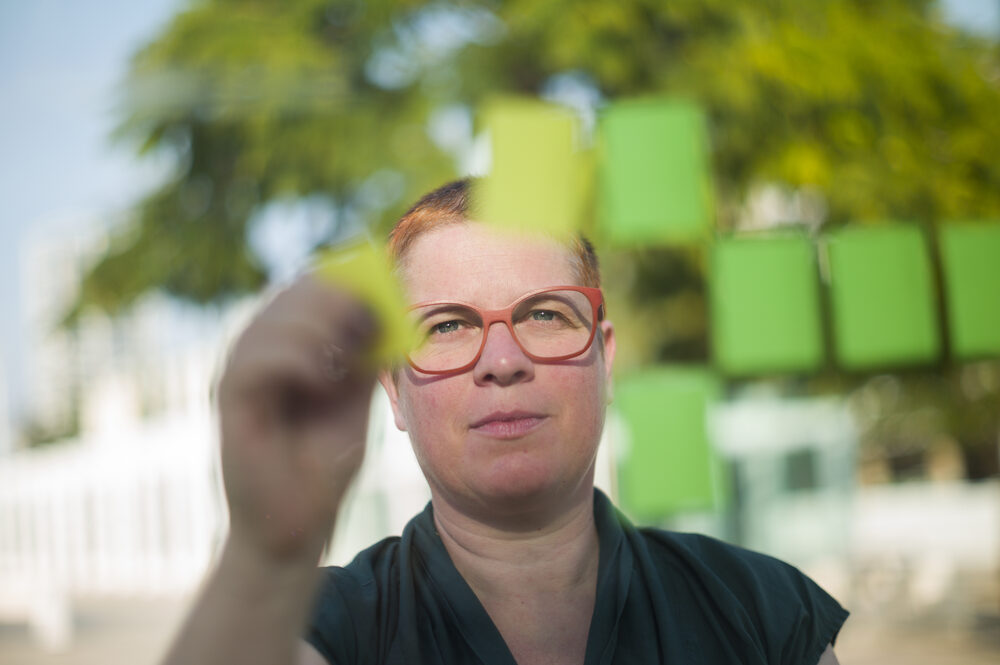 Nadja ordnet grüne Haftnotizen an einer Glaswand